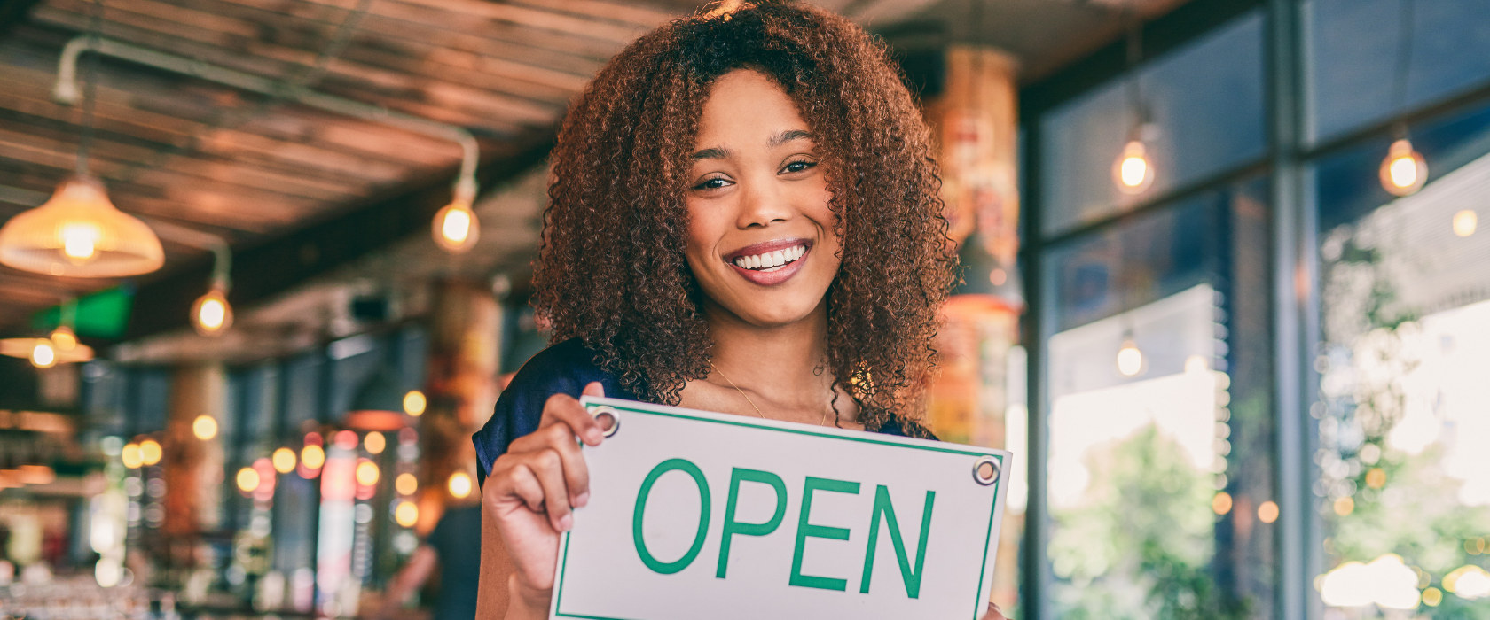 young female business owner holding up an open sign at her new business
