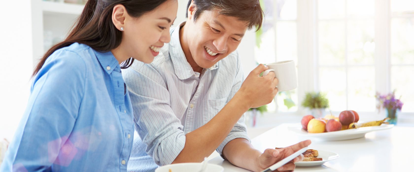 Happy couple looking at a tablet at their kitchen counter at home