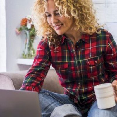 Woman on her computer using online & mobile banking on her couch with a cup of coffee