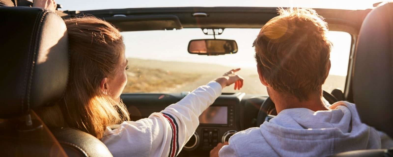 young couple driving a jeep with the top-down pointing at something in the distance