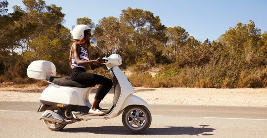 white scooter driven by a young woman going down the highway.